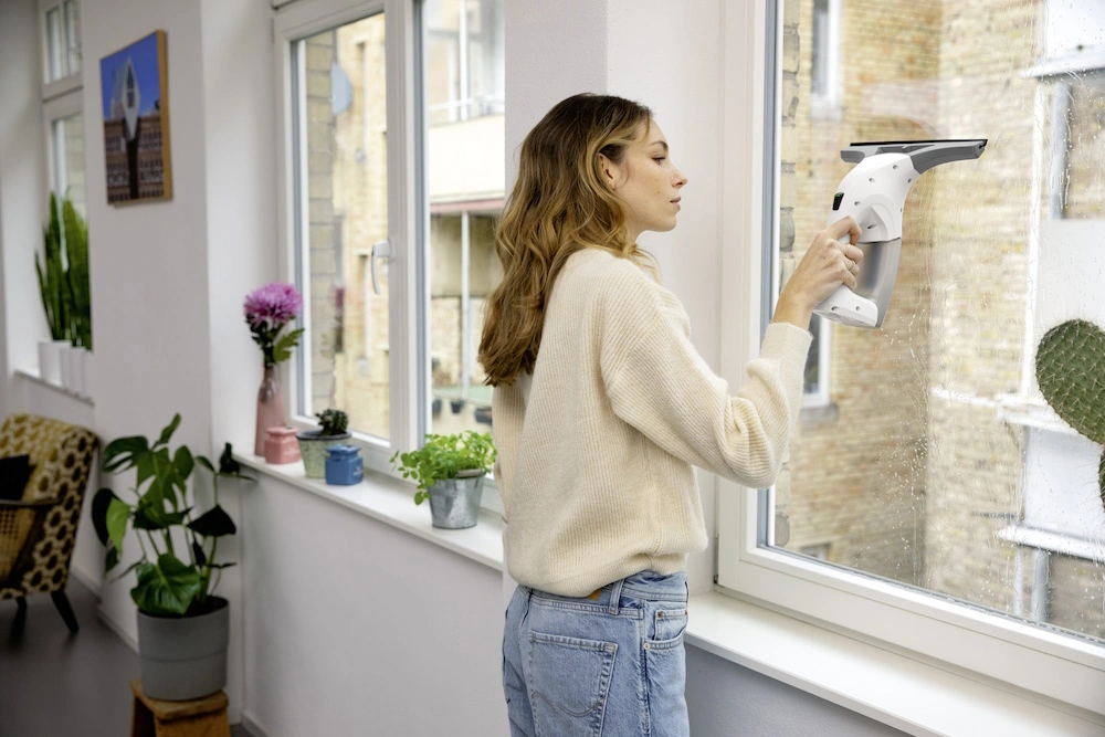 Eine Person reinigt ein Fenster mit einem Kärcher Fensterreiniger